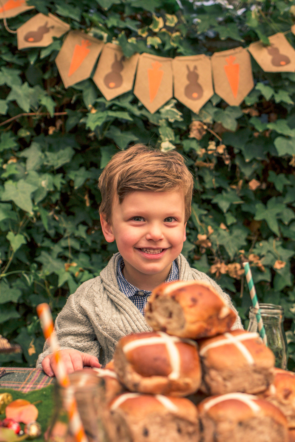 Little boy eating hot cross buns at kids party table at Autumn easter egg hunt