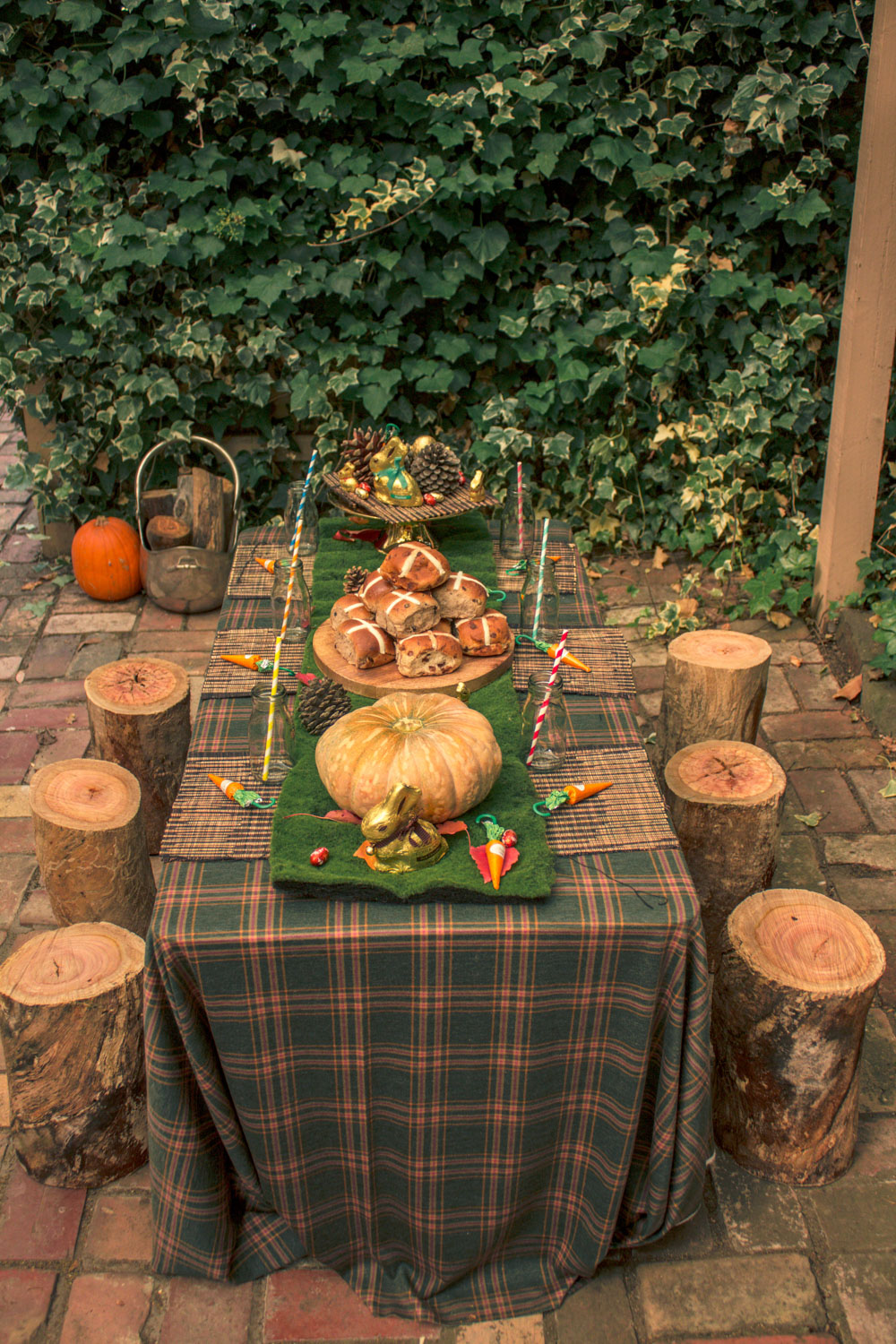 Children easter table for autumn themed easter egg hunt. Table decorated with pumpkins, hot cross buns, pine cones and chocolate carrots and wooden log stools