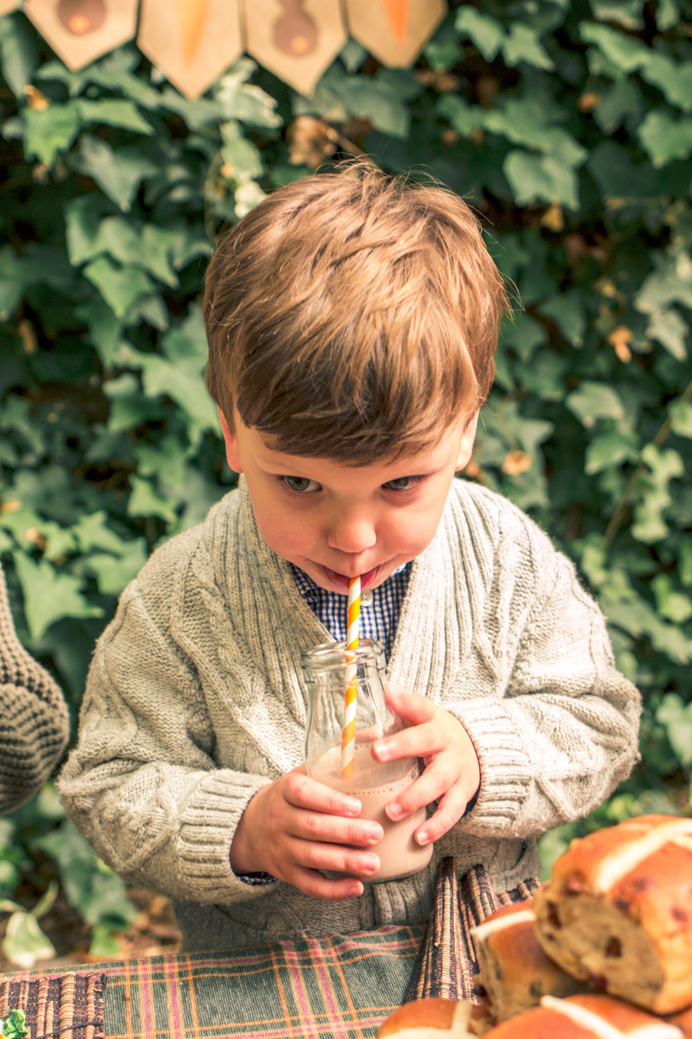 Little boy wearing vintage knit cardigan from Janie and Jack drinking chocolate milk  from glass milk bottle with organ and white stripes at party table for autumn easter egg hunt