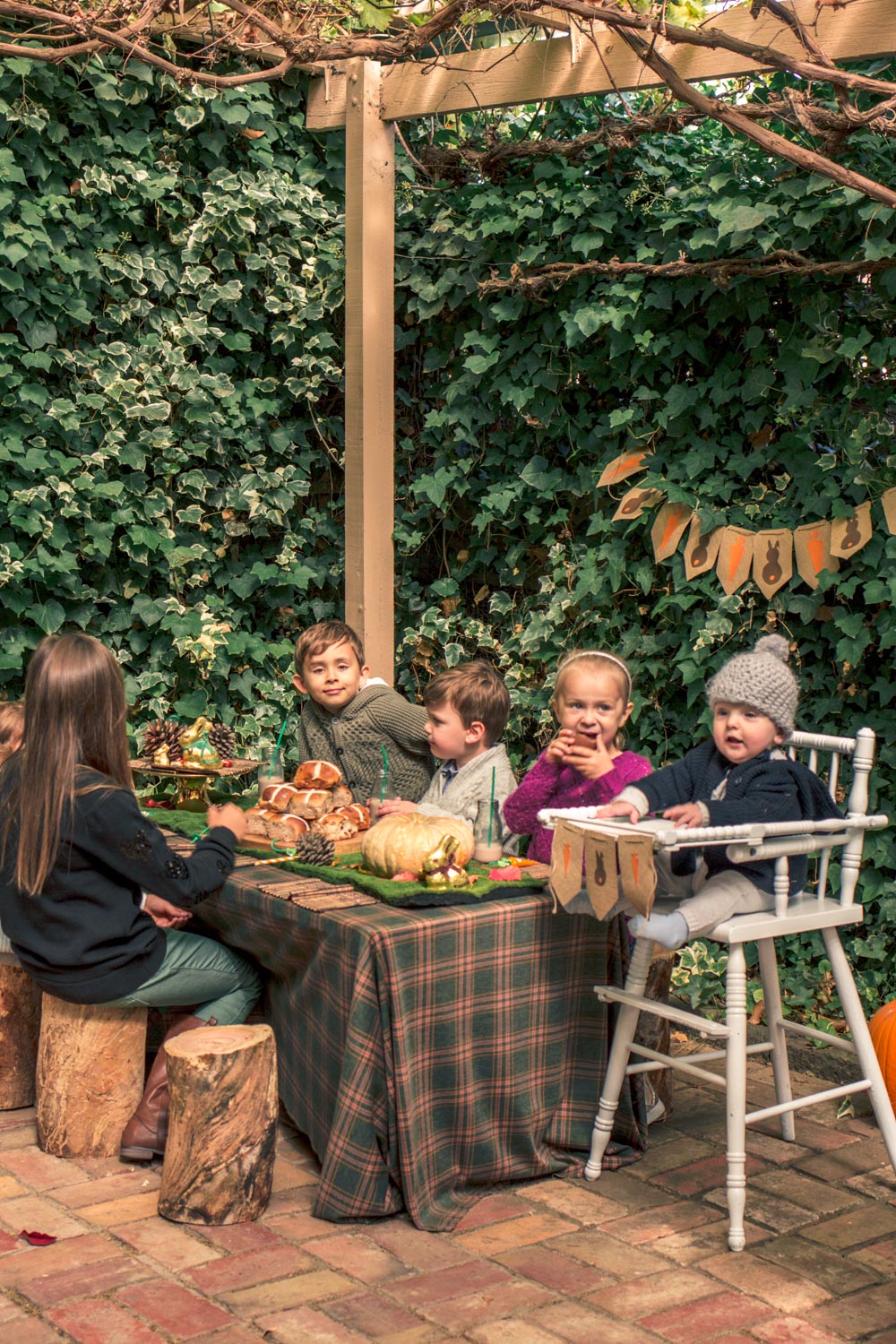 Kids seated at children party table for autumn easter breakfast at autumn easter egg hunt. Table decorated with woodland themed pine cones, pumpkins, chocolates and hot cross buns.