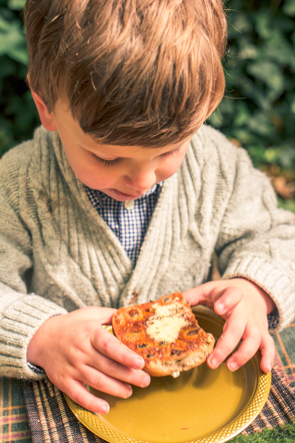 Little boy in knit cardigan eating a hot cross bun at easter table