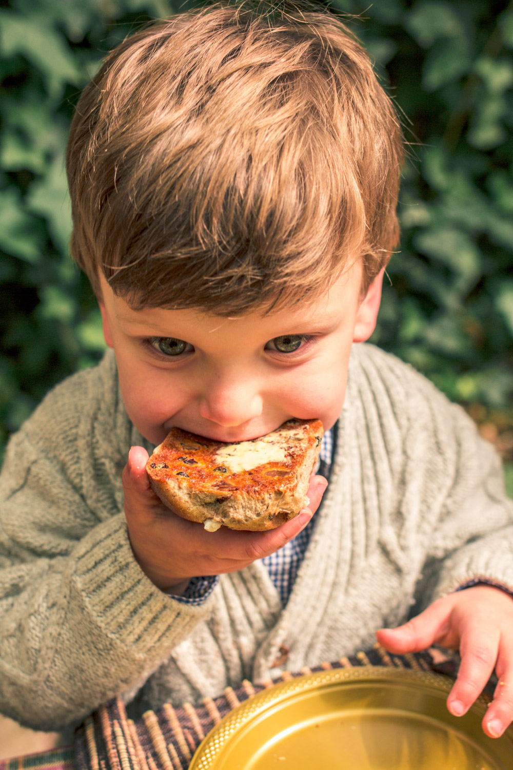 Little boy wearing a knit cardigan eating a Bakers Delight Hot Cross Bun at Autumn Easter Egg Hunt