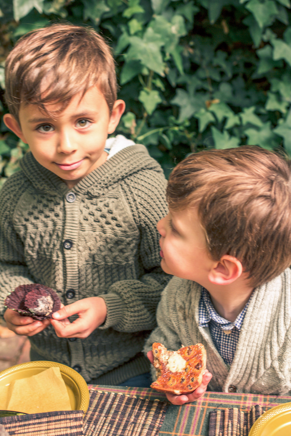 Little boys dressed in knit cardigans eating hot cross buns at autumn easter egg hunt party