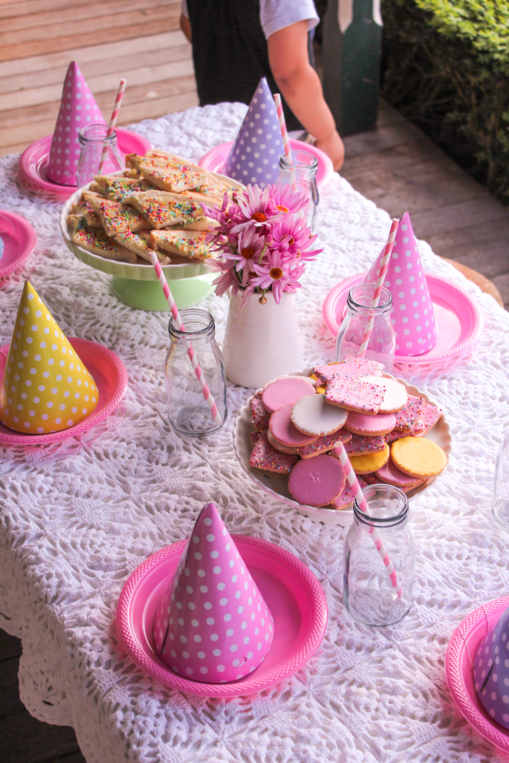 Spring themed kids table with pink polka dot party hats, straws, fairy bread and cookies