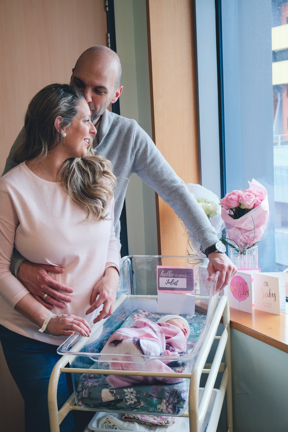 Goldfields Girl sitting in hospital window with new baby surrounded by flowers and cards