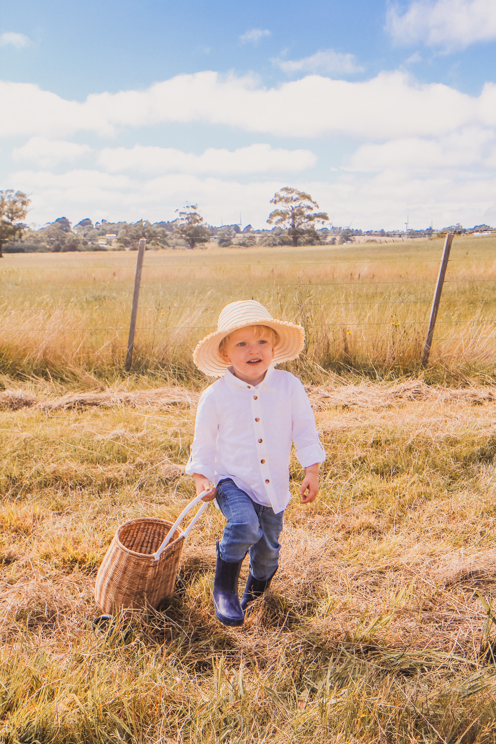 Little boys wearing linen shirts straw hats and Olli Ella luggy at sunflower farm near Ballarat