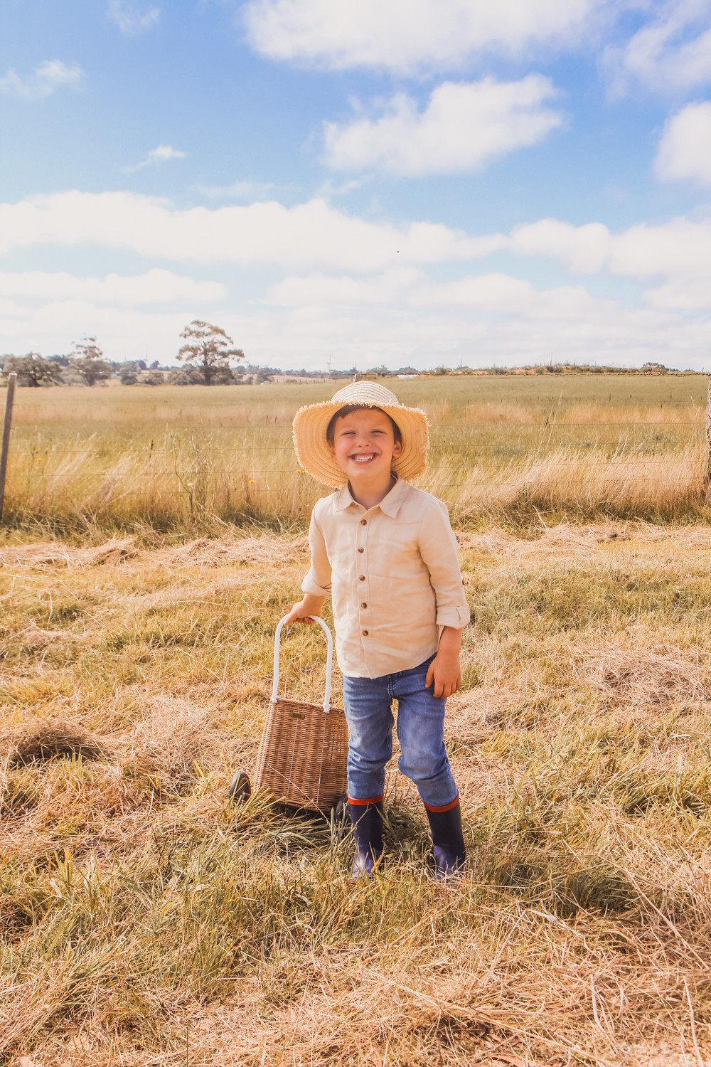 Little boys wearing linen shirts straw hats and Olli Ella luggy at sunflower farm near Ballarat