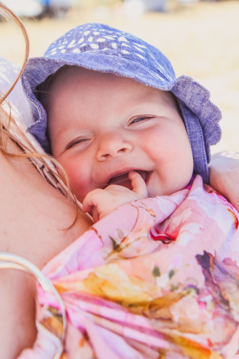 Baby sitting in pink ring sling baby carrier amongst sunflower field