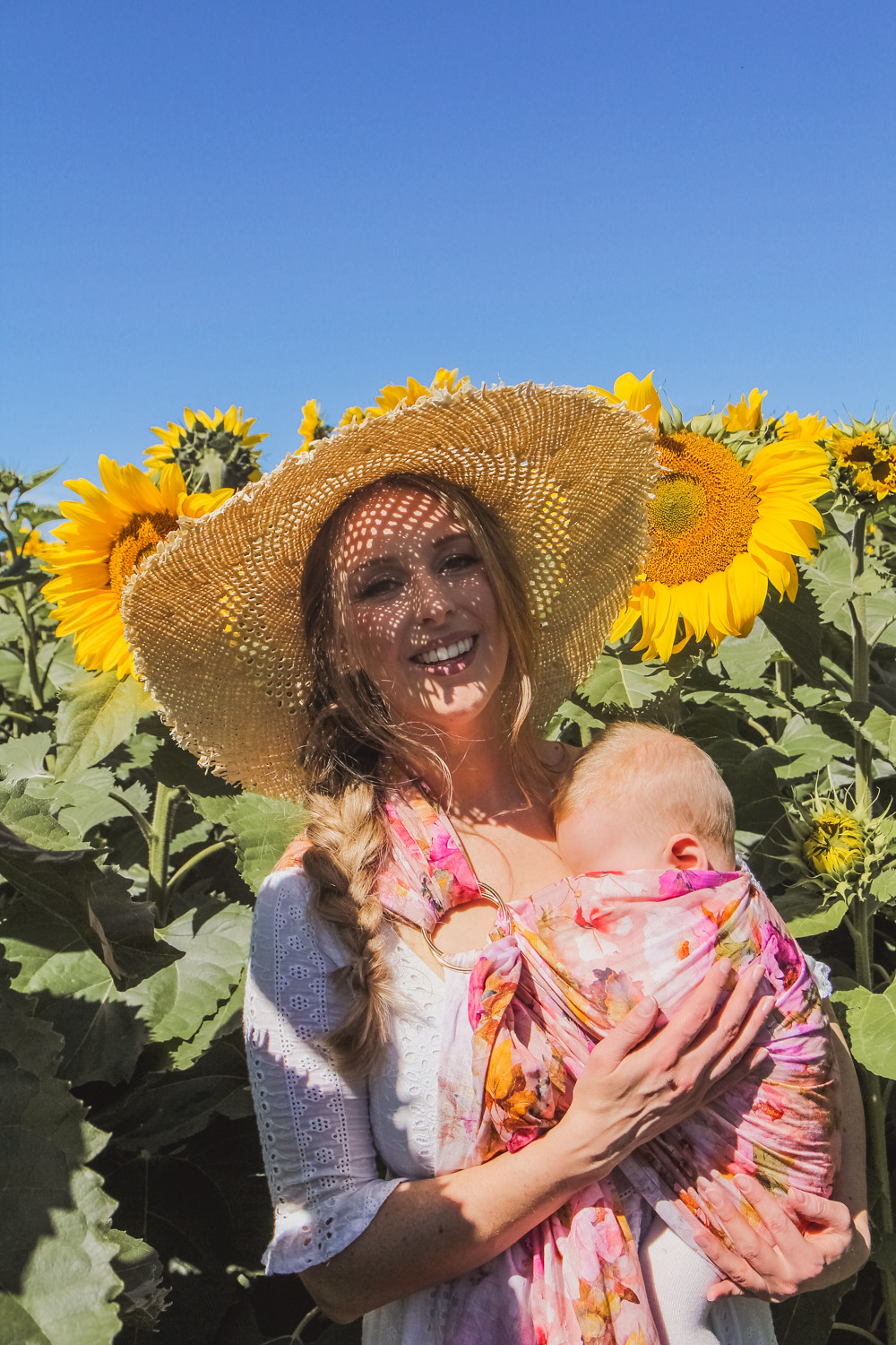 Goldfields Girl at sunflower farm in Ballarat in Victoria. Wearing white eyelet dress, straw hat and ping ring sling baby carrier.