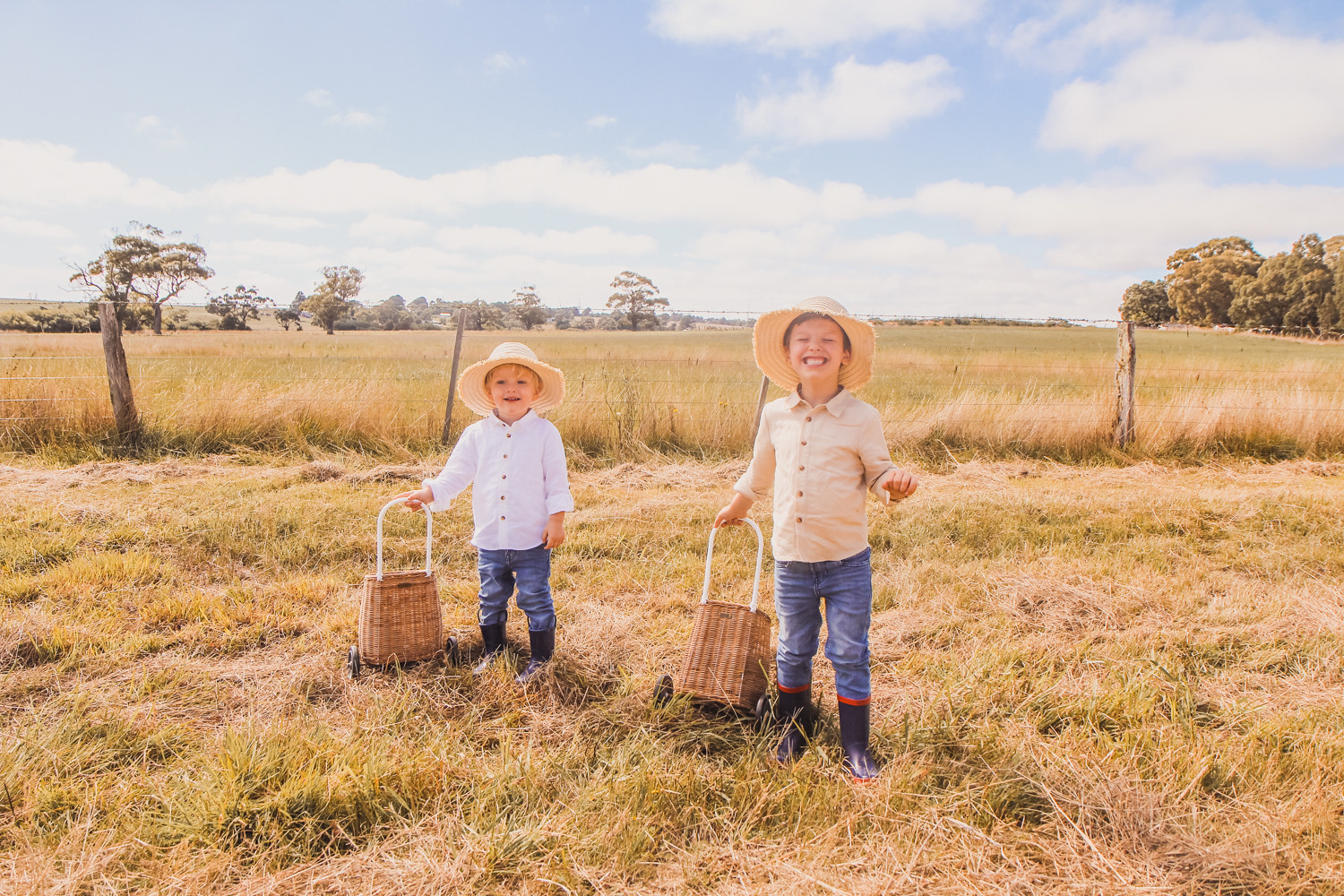 Little boys wearing linen shirts straw hats and Olli Ella luggy at sunflower farm near Ballarat