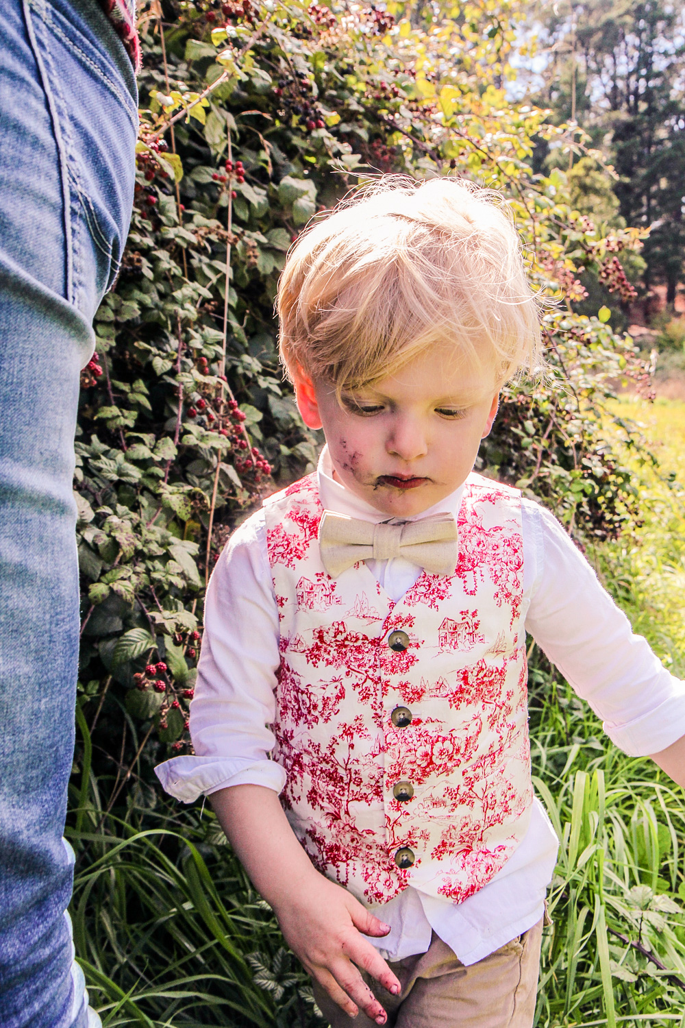 little boy wearing red toile vest and bow tie with blackberry juice on his face