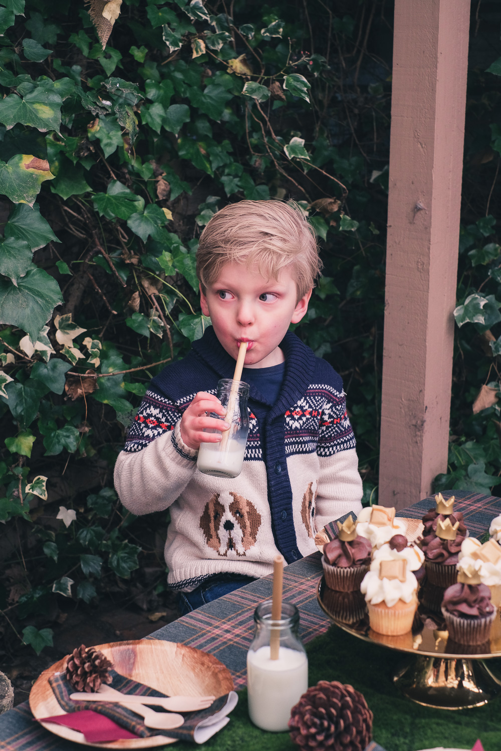 Little boy seated at party table drinks from a milk bottle with eco bamboo straw