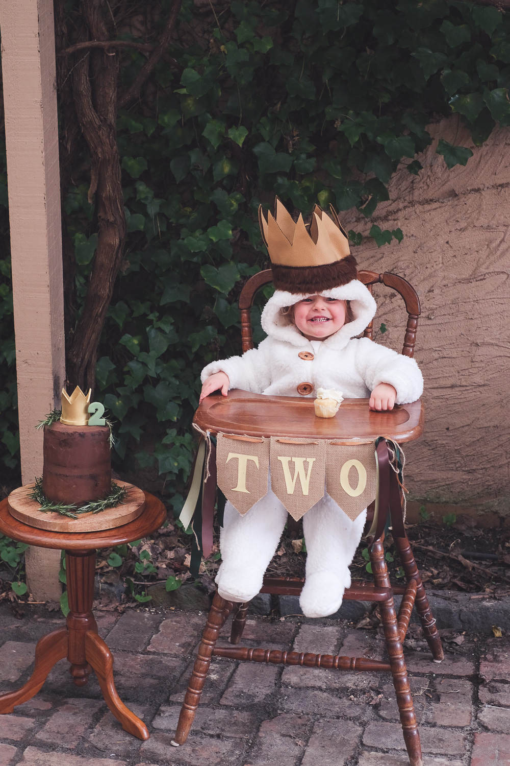 Child wearing Where The Wild Things Are party costume sits in a vintage high chair next to birthday cake